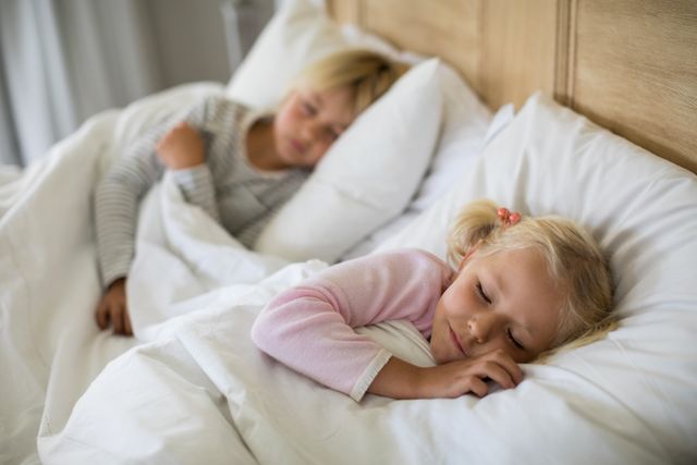 Two children are sleeping peacefully in a cozy bed at home. They are resting comfortably under white blankets, creating a serene and tranquil atmosphere. This image can be used for themes related to childhood, family life, bedtime routines, and the importance of sleep. Ideal for parenting blogs, sleep aid products, and family-oriented advertisements.