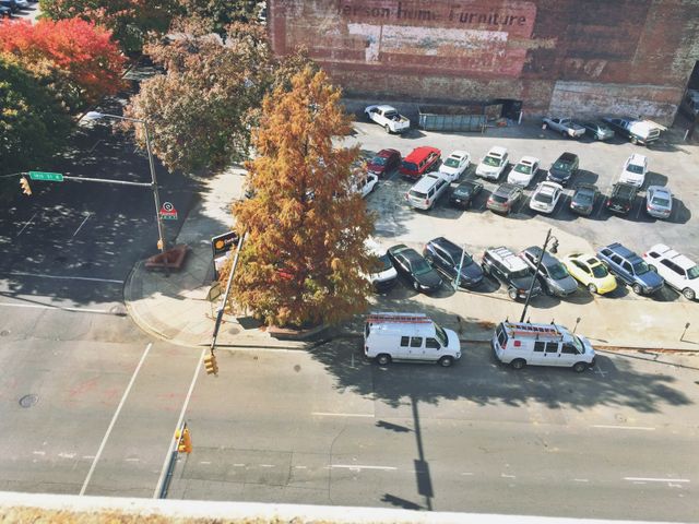 Overhead view of an urban street and parking lot during daytime. Trees show autumn colors. Ideal for urban planning, seasonal themes, or city life concepts.