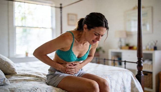Young woman clutching abdomen on bed experiencing abdominal pain and morning discomfort
