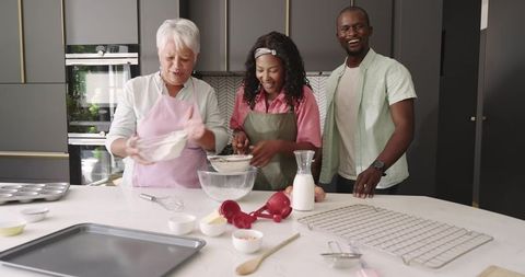 Multigenerational family baking together in modern kitchen, smiling and sifting flour