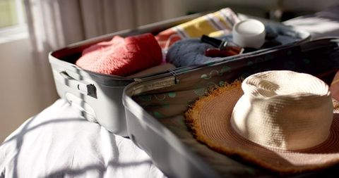 Open suitcase filled with clothes and straw hat for tropical vacation
