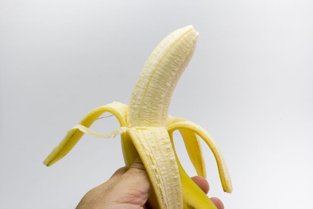 Peeled banana held in hand against white background. Suitable for topics on healthy eating, fresh fruits, tropical fruits, and minimalistic designs. Ideal for nutrition blogs, health articles, food industry content, and advertising materials.