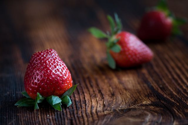 Freshly picked strawberries placed on a rustic wooden surface. The shallow depth of field highlights the freshness and organic nature of the strawberries. Great for use in food blogs, nutrition articles, advertisements for fresh produce, or farmhouse-themed decor.