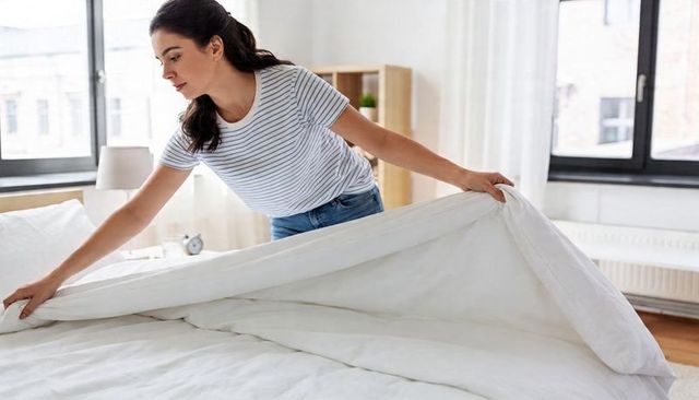 Woman smoothing white duvet in bright minimal bedroom, making bed, home routine