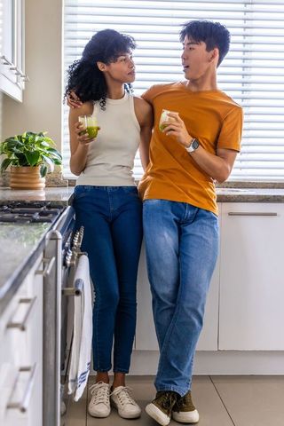 African american woman and asian man leaning on kitchen counter holding green smoothies