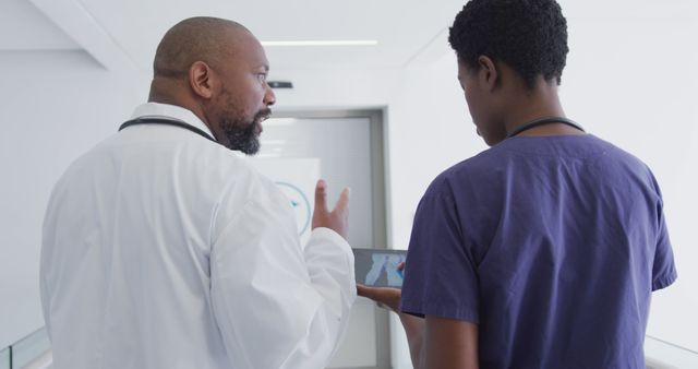African american male and female doctors using tablet, talking at hospital. Medicine, healthcare, lifestyle and hospital concept.