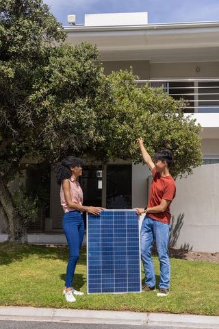 Diverse couple holding solar panel assessing roof shade planning home solar install