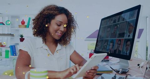 Smiling woman working on tablet in bright home office joining virtual team on monitor