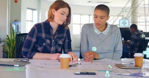 Two women collaborating on large-format plans in modern office