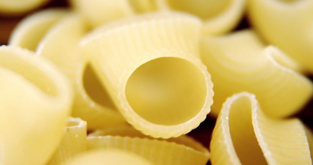 Close-up view of paccheri pasta. Paccheri is a large, tube-shaped pasta that is popular in Italian cuisine. This zoomed-in perspective highlights the texture and structure of the pasta, with its ribbed exterior creating visual interest. This image can be used for culinary blogs, Italian recipe books, cooking websites, or food product packaging.