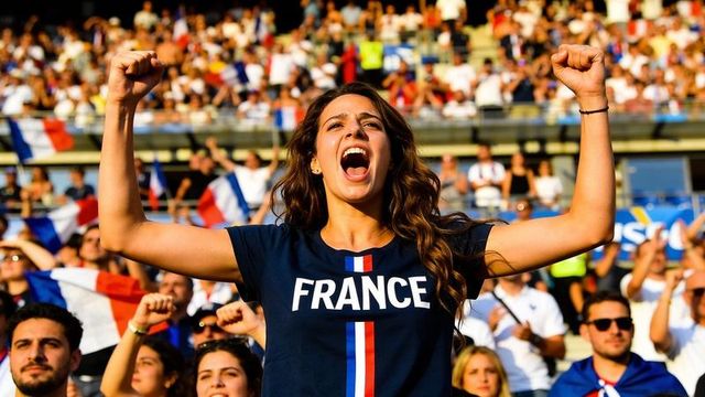 Passionate french fan cheering with raised fists wearing france tee in stadium crowd