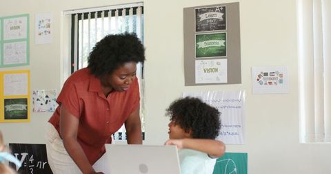 African american teacher guiding student using laptop in classroom mentoring and learning