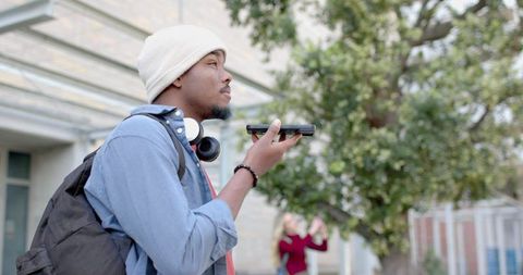 African american student speaking into smartphone wearing backpack and headphones on campus