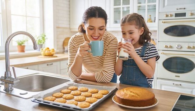 Mother and daughter enjoying homemade cookies and milk in bright kitchen with morning sun