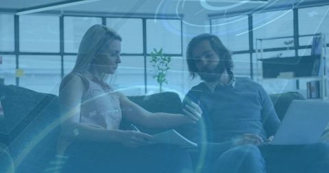 Colleagues reviewing documents on sofa with laptop and smartphone in modern office