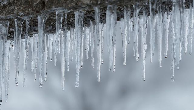 Dripping icicle fringe on ice-coated rock ledge with clear water droplets, winter texture