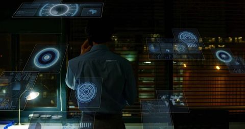 Businessman monitoring holographic data dashboards in late-night office using smartphone