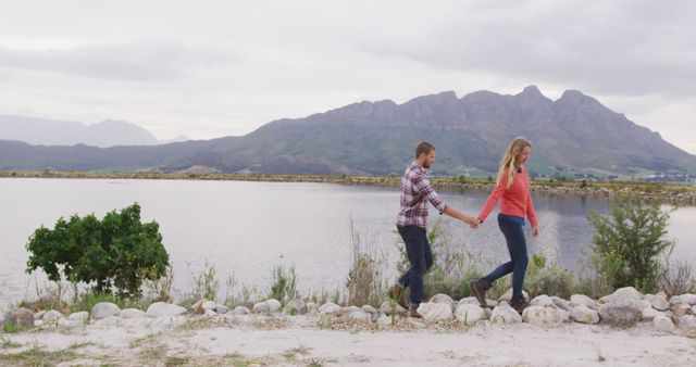 Caucasian couple walking by lake holding hands with copy space. Nature, travel, tranquility, lifestyle concept, unaltered.