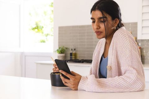 Woman Engaged on Smartphone While Eating at Kitchen Table