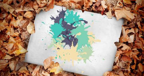 Colorful paint splatters on paper amidst autumn leaves