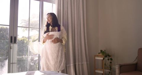 Mother Holding Swaddled Infant Near Sunlit Doors