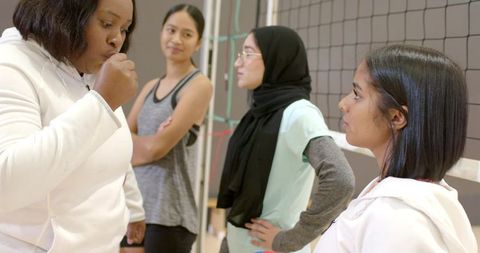 African american coach guiding diverse girls volleyball team during practice in gym