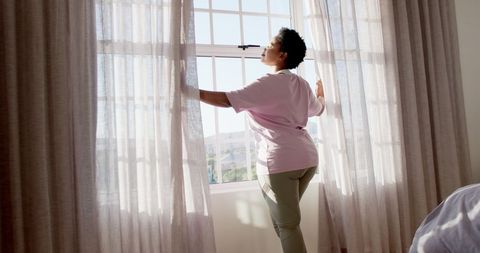 African American Woman Opens Curtains to a Sunlit Room - Download Free Stock Images Pikwizard.com