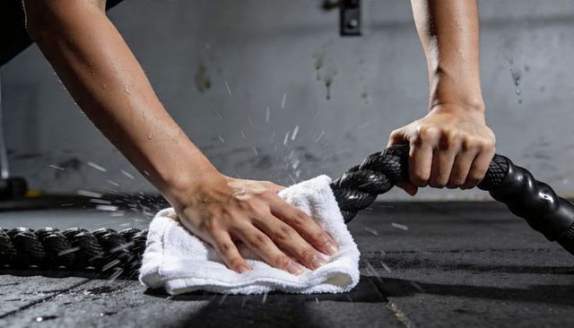 Sweaty forearms gripping battle rope rubbing towel during intense gym workout for strength