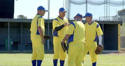 Sunlit amateur baseball team huddling by dugout in yellow uniforms with gloves