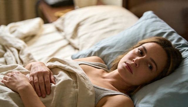 Woman lying in bed with linen sheets and blue pillow relaxing morning calm