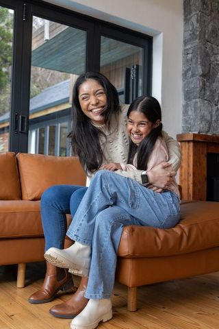 Mother and daughter laughing and hugging on leather sofa in cozy rustic living room