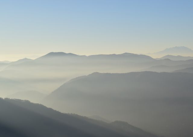 Capturing the quiet beauty of a mountain range at dawn, enveloped in gentle fog. Ideal for backgrounds, nature blogs, travel content, and meditation resources promoting serenity and tranquility.
