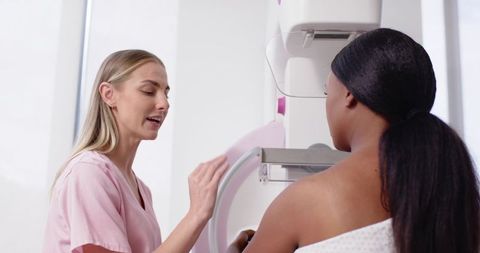 Female technologist guiding patient during mammography breast screening in clinic