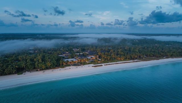 Dawn mist over tropical beachfront villas with palm trees and turquoise sea