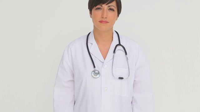 A female doctor confidently stands looking at the camera against a light grey background, wearing a white coat and a stethoscope. She exemplifies professionalism and dedication, suitable for any healthcare-related content, medical articles, or healthcare advertisement. Ideal for showcasing female representation in the medical field or enhancing marketing material for clinics and hospitals.