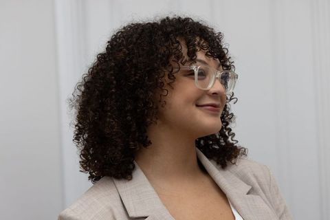 Confident professional woman with curly hair wearing clear eyeglasses and beige blazer