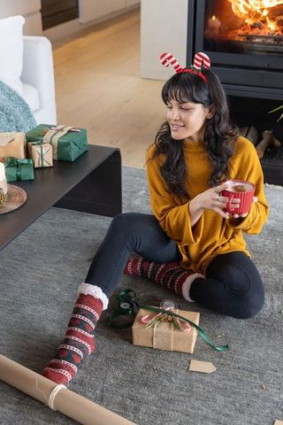 Woman relaxing during holiday gift wrapping with winter socks and mug