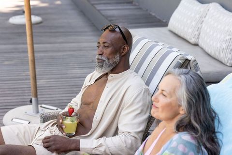 Mature diverse couple relaxing on resort deck sipping tropical cocktail by pool