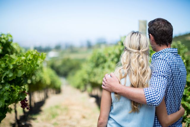 Couple embracing while enjoying a sunny day at a vineyard. Ideal for advertisements, travel blogs, romantic getaways, winery promotions, agricultural tourism, or any content focusing on love, nature, and tranquility.