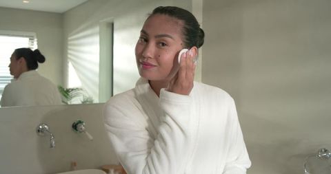 Asian woman applying toner with cotton pad during morning skincare routine in minimalist bathroom