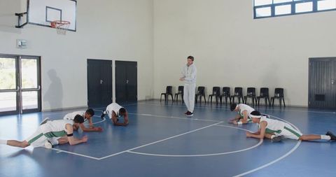 Basketball coach supervising team stretching in gym