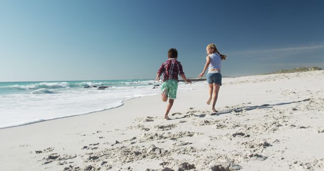 Caucasian girl and boy running on beach by seaside, copy space. Childhood, lifestyle, vacation, summer, happiness, wellbeing concept, unaltered.