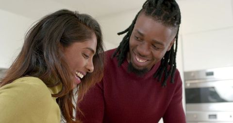Mixed-Race Couple Laughing in Modern Kitchen, Leaning Close, Sharing Warm Moment in Casual Sweaters