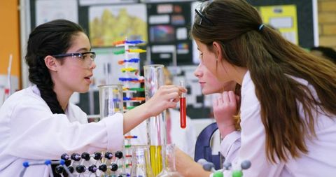 Teen girls conducting hands-on chemistry experiment in high school science classroom