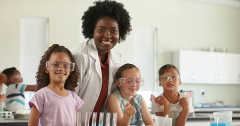 African american teacher leading girls in hands-on science experiment with goggles