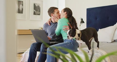 Happy couple multitasking with laptop and dog in cozy bedroom