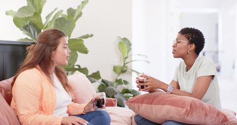 Multiracial friends chatting over coffee on sunlit sofa with pink cushions