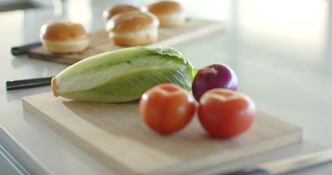 Romaine lettuce and tomatoes with red onion prepping sandwich ingredients on bright kitchen counter