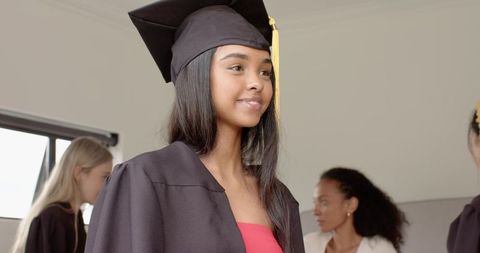 Young Asian woman graduating wearing cap and gown with yellow tassel and red dress smiling