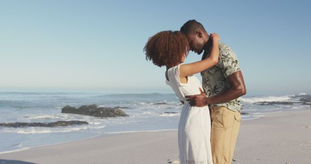 Romantic couple embracing on a beach during a sunny day with ocean waves in the background. Perfect for themes related to love, romance, vacations, and leisure activities. Could be used in advertisements, travel brochures, relationship blogs, or greeting cards.